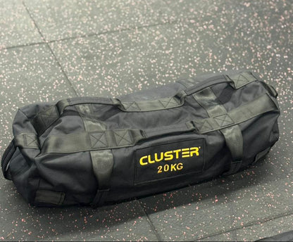 Black sand bag labeled 'Cluster 20KG' on a textured floor for Hyrox Training