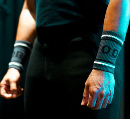 Person wearing black wristbands with 'REWOD' branding, standing against a dark background.