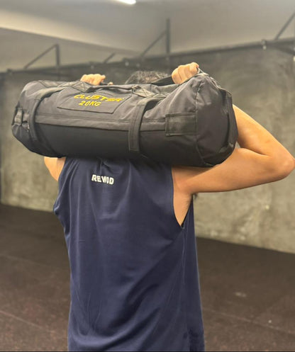 Person carrying a cluster sand bag labeled '20kg' on their back in an indoor setting.